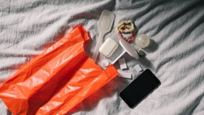 Embalagem laranja aberta sobre a cama com pequenos produtos e um celular ao lado